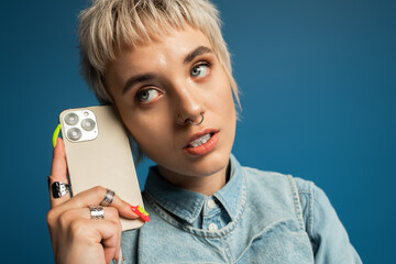 Stylish young woman with edgy haircut conversing on smartphone against vibrant backdrop