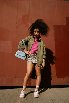 Trendy retro streetwear model posing outdoors with afro hair and bag