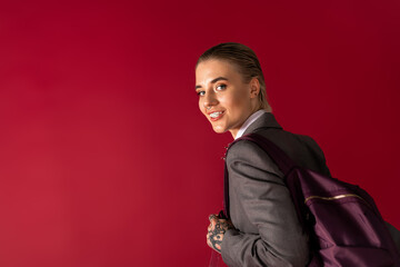 Stylish young woman with a backpack smiles confidently against a vibrant red backdrop