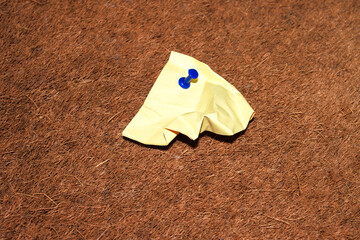 Wrinkled sticky note with pushpin on cork bulletin board in office or school