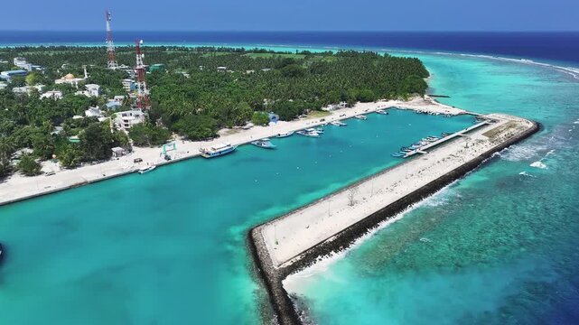 Aerial view of the vibrant turquoise harbor of Thoddoo, where boats rest near the shore, contrasting with the island's lush greenery, Thoddoo, Alif Alif Atoll, Maldives.