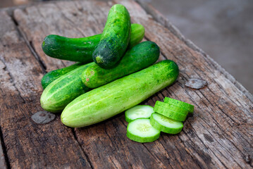 cucumber (Cucumis sativus) and slices on wood background. Freshly sliced mini cucumbers with knife on wooden cutting board.
