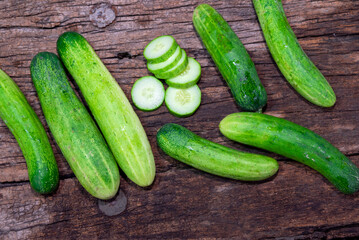 cucumber (Cucumis sativus) and slices on wood background. Freshly sliced mini cucumbers with knife on wooden cutting board.