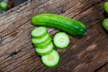 cucumber (Cucumis sativus) and slices on wood background. Freshly sliced mini cucumbers with knife on wooden cutting board.