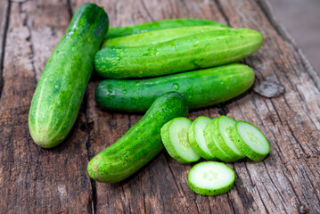 cucumber (Cucumis sativus) and slices on wood background. Freshly sliced mini cucumbers with knife on wooden cutting board.