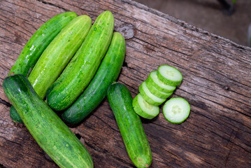 cucumber (Cucumis sativus) and slices on wood background. Freshly sliced mini cucumbers with knife on wooden cutting board.