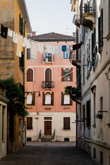 Picturesque narrow street in Venice with hanging laundry, pastel facades, rustic balconies, and a pink building at the end of the alley, showcasing the timeless character of Italian cities