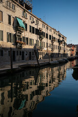 Historic Venetian houses reflecting in the calm canal water at sunset, creating a mirror-like scene that emphasizes the timeless beauty and architectural harmony of Venice