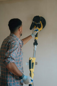 Man sanding wall with electric tool during house renovation indoors