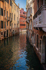 Narrow Venetian canal lined with colorful old buildings, reflections shimmering on the water, and a peaceful glimpse of daily life in Italy’s historic floating city