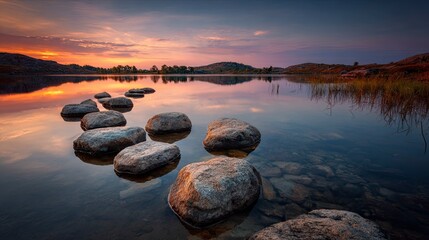 Serene Sunset Over Calm Lake with Large Rocks in Foreground and Mountainous Horizon