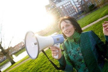 Woman with megaphone smiling in park on a sunny afternoon