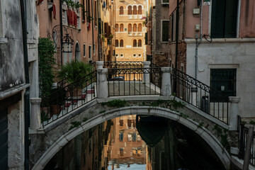 Fototapeta premium Charming pedestrian bridge in Venice with canal reflections and pastel facades, symbolizing daily lifestyle, urban exploration and romantic travel experiences in Italy’s floating city