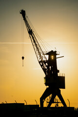 Towering crane outlined by warm evening light at harbor skyline, symbolizing shipping culture,...