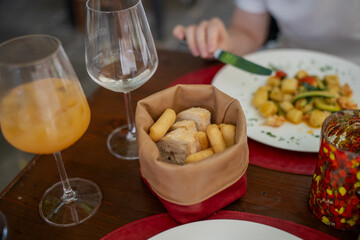 Dining table with basket of Italian breadsticks and focaccia, glassware, colorful condiments and plate of gnocchi pasta with vegetables served in Mediterranean restaurant