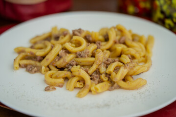 Traditional Italian comfort food with pasta and rich meat sauce presented simply on plate, representing rustic Mediterranean dining culture, heritage cooking and travel eating