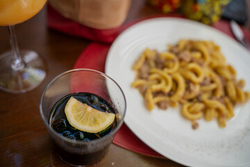 Authentic Mediterranean dining scene with hearty pasta dish, refreshing drink, citrus garnish and casual table setting reflecting Italian culture, travel and gourmet lifestyle