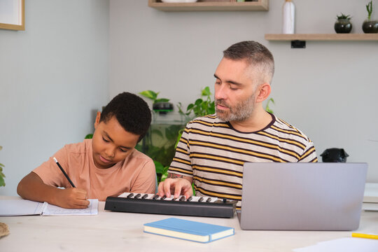 Father teaching son music with piano keyboard and notebook at home