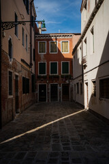 Atmospheric street view in Venice with contrasting light and shade on colorful facades and old stone pavement, capturing quiet charm and authentic character of Italian old town