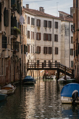 Scenic Venice canal view with small boats, historic houses and wooden bridge in background, showcasing authentic charm, atmospheric lifestyle and cultural heritage of Italian city