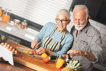 Happy mature couple using touchpad while preparing food in the kitchen