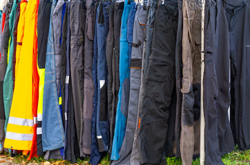 Flea market with used workwear hanging on racks, various colors and styles of protective trousers,...