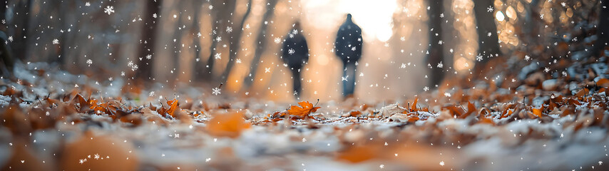 Obraz premium Autumn leaves and first snowflakes settle on a forest trail as hikers pass—capturing the quiet transition between seasons in warm golden hour light.