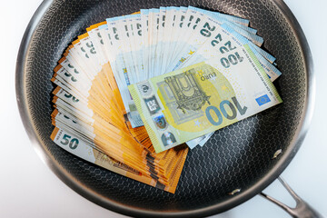 Stacks of euro banknotes placed inside a frying pan, symbolizing money, finance, savings,...