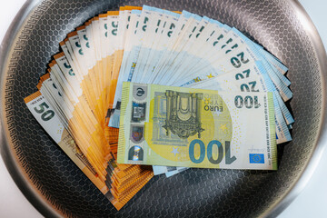Stacks of euro banknotes placed inside a frying pan, symbolizing money, finance, savings,...