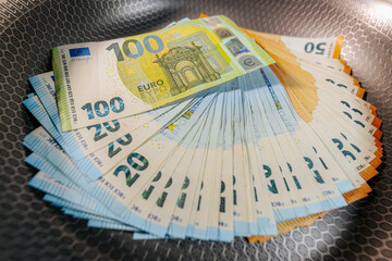 Stacks of euro banknotes placed inside a frying pan, symbolizing money, finance, savings,...