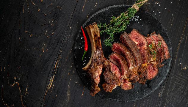 Sliced grilled tomahawk steak with herbs and spices on dark wooden background, top view, copy space