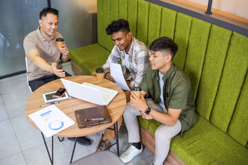 Three Diverse Young Men Engaged in Productive Meeting Looking at Laptop While Having Coffee