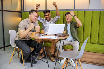 Diverse Young Men Celebrating Success With Their Fists Raised While Working on Laptop