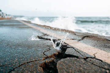 Cracked asphalt road with seawater splashing upward during storm surge