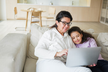 Mother and daughter enjoy laptop time together on cozy couch