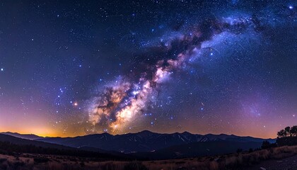 Naklejka premium A brilliant night sky filled with stars and the glowing Milky Way galaxy arching over a remote mountain landscape panorama