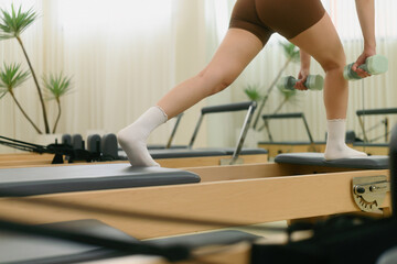 Close-up of powerful leg and glute activation as a woman performs a lunge with dumbbells on a reformer machine in a sleek, modern Pilates studio