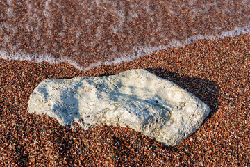 big beautiful white stone lies on coastline and small stones of beach of Adriatic Sea, with beautiful foaming wave, as abstract background of summer travel and vacation