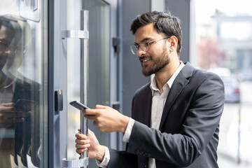 Indian businessman scanning smartphone at office entrance to unlock door with nfc contactless access, showcasing secure, modern mobile authentication for corporate building access control