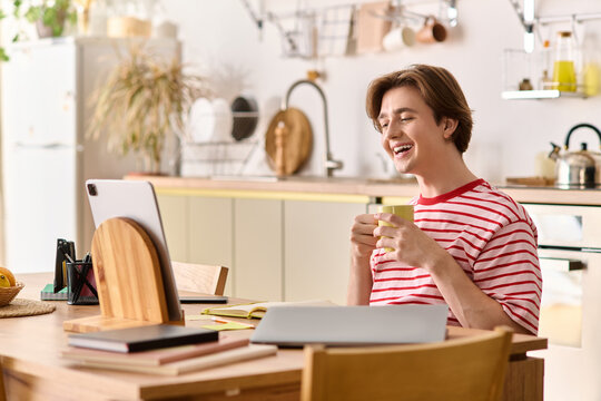 Young man enjoys studying online while sipping tea in his cozy modern apartment - Powered by Adobe
