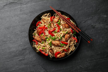 Tasty noodles with chicken, green onions and vegetables served on black table, top view