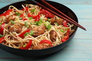 Tasty noodles with chicken, green onions and vegetables served on blue wooden table, closeup