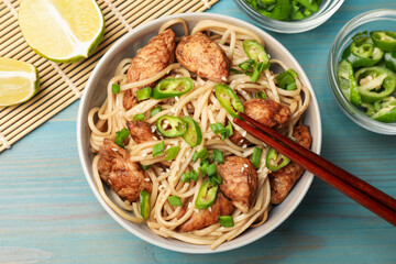 Tasty noodles with chicken, green peppers and sesame seeds served on blue wooden table, flat lay