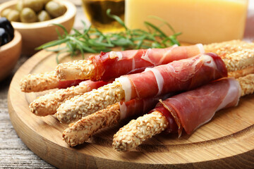 Delicious grissini sticks with sesame seeds and prosciutto on wooden table, closeup