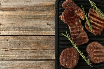 Delicious grilled beef meat with rosemary on wooden table, top view. Space for text