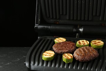 Electric grill with beef and zucchini on black table, closeup