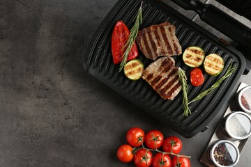 Electric grill with beef steaks, vegetables and rosemary on grey table, flat lay. Space for text