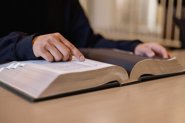 Man reading large book with finger pointing on page at library desk. Concept of studying, education, research, knowledge, learning process, academic preparation, intellectual development.