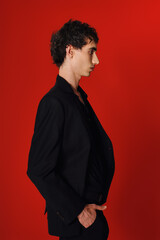Obraz premium Handsome man showcases elegant fashion against a striking red backdrop