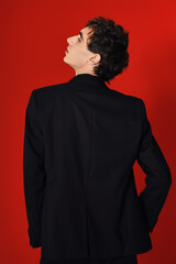 Stylish man in elegant black attire poses confidently against a vibrant red background
